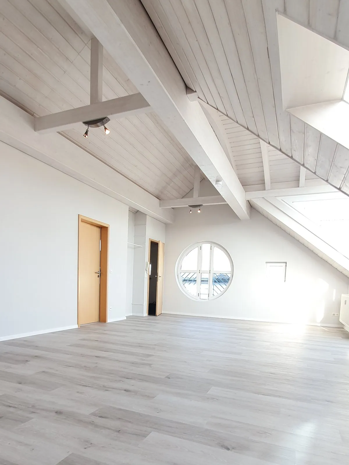 Heller Dachgeschossraum mit sichtbarem Balkenwerk und rundem Sprossenfenster