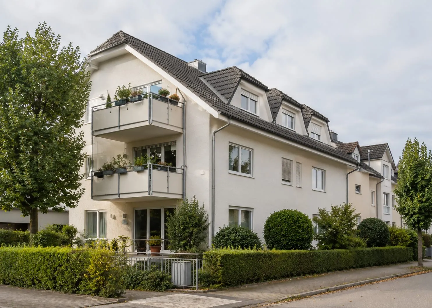 Mehrfamilienhaus mit Balkonen und Hecke an einer Wohnstraße