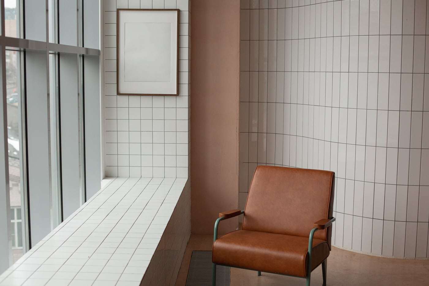 Brauner Ledersessel am Fenster vor einer weiß gefliesten Wand