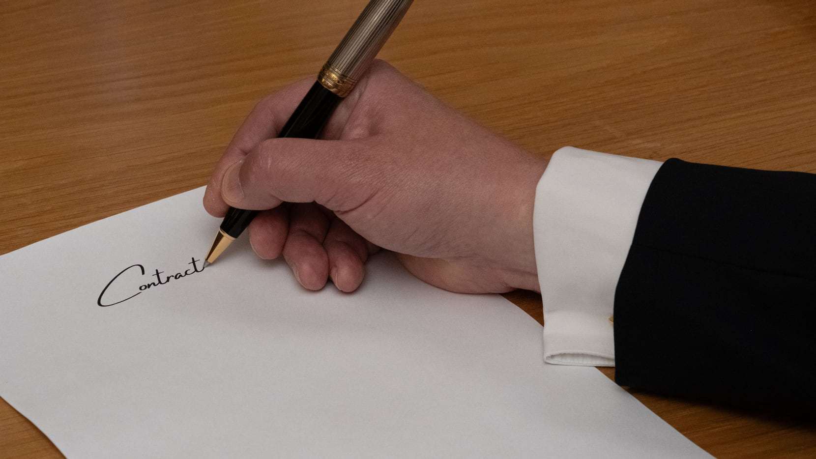 Hand im Anzug unterschreibt mit einem Füller auf hellem Papier