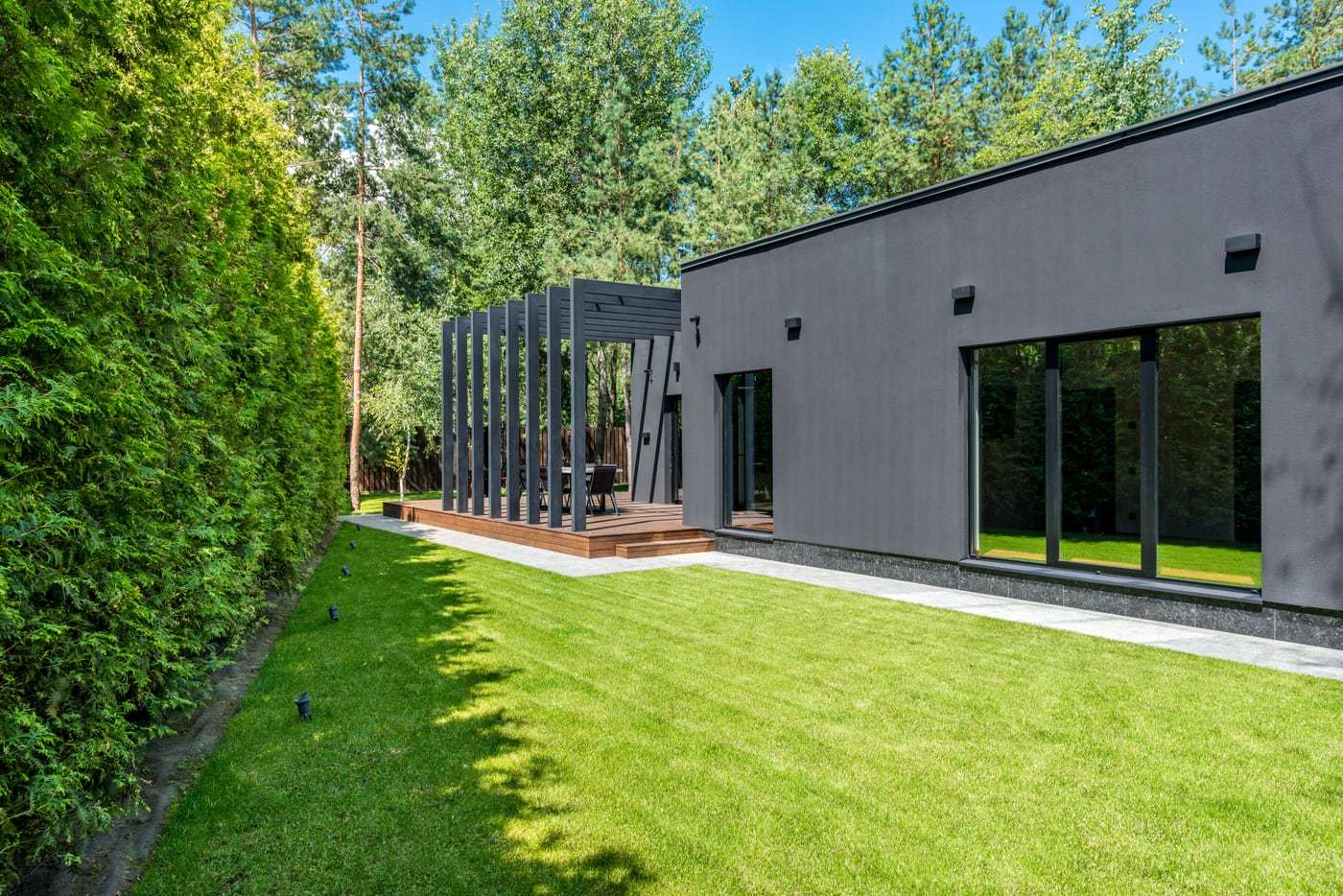 Moderner grauer Flachdachbungalow mit Rasen und hoher Hecke