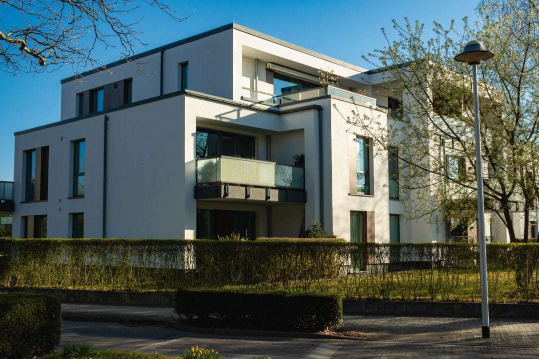 Modernes weißes Mehrfamilienhaus mit Dachterrasse hinter einer Hecke