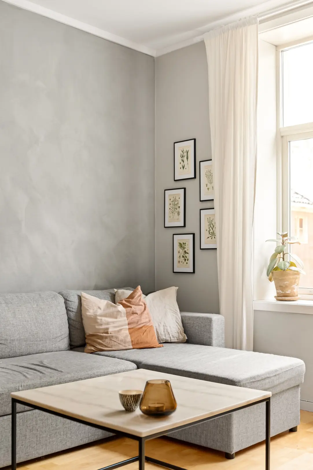 Wohnecke mit grauem Sofa, Couchtisch und Bilderrahmen am Fenster im Tageslicht